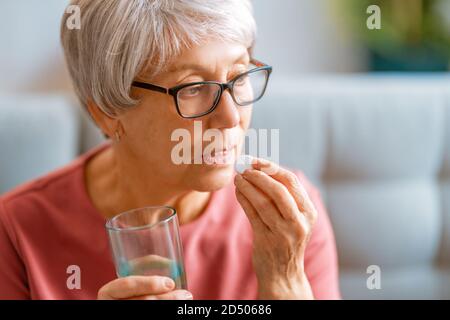 Femme âgée tenant une pilule et un verre d'eau douce, prenant des médicaments contre les maux de tête, les douleurs à l'estomac ou prenant des vitamines, des médicaments de sédation. Banque D'Images