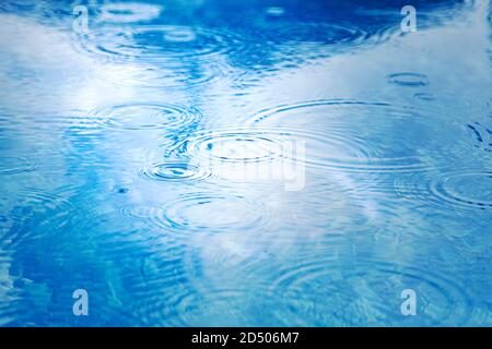 Gouttes de pluie sur la surface de l'eau bleu de la piscine. Texture de l'eau bleue comme arrière-plan. Taches les cercles sur l'eau de la pluie Banque D'Images