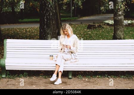 jeune femme d'affaires assise sur le banc dans le parc d'automne et parlant au téléphone en prenant des notes. Pause-café à l'extérieur. Banque D'Images