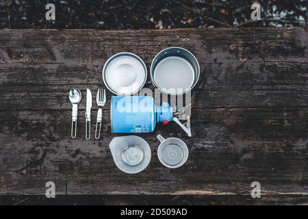 Le camping, le tourisme et les équipements de voyage avec cuisinière à gaz, pot et couverts sur une table en bois. Banque D'Images