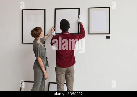 Vue arrière portrait de deux ouvriers de galerie d'art accrochant des cadres de peinture sur le mur blanc tout en planifiant l'exposition dans le musée, espace de copie Banque D'Images