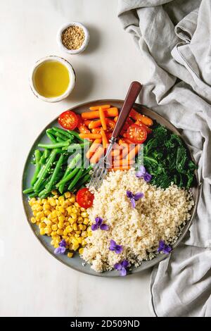 Couscous aux légumes étuvé bébés carottes, haricots verts, épinards, maïs sucré servi dans une plaque en céramique avec des tomates, de sésame et de fleurs comestibles. Ve Banque D'Images