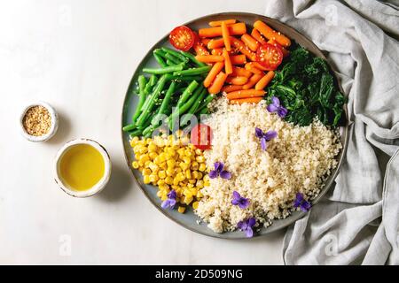 Couscous aux légumes étuvé bébés carottes, haricots verts, épinards, maïs sucré servi dans une plaque en céramique avec des tomates, de sésame et de fleurs comestibles. Ve Banque D'Images