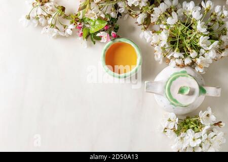 Fait main artisanat théière et tasse en céramique avec du thé chaud décoré par cherry blossom printemps branches sur fond de marbre blanc. Mise à plat, de l'espace Banque D'Images