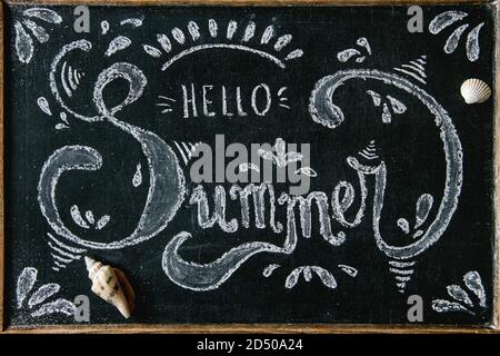 Thème d'été. Lettrage décoratif à la craie manuscrite Bonjour été sur tableau noir, décoré par coquillages Banque D'Images