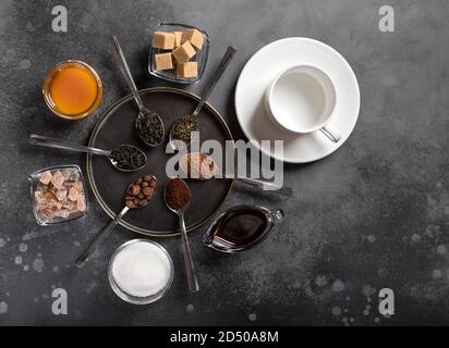 différents types de thé (noir, vert, à base de plantes), café (moulu, haricots, cacao), édulcorants (sucre, miel, sirop de dattier) et tasse blanche vide. fond sombre Banque D'Images