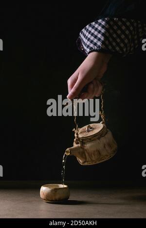 Jeune homme de de l'artisanat faits à la main chaude dans la théière de thé vert chinois traditionnel tasse en céramique argile debout sur le tableau sombre sur fond noir Banque D'Images