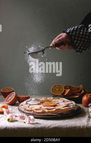 La main du jeune homme du sucre en poudre d'arrosage des Cheesecake avec orange sanguine de Sicile, décoré par des fleurs comestibles, les feuilles de menthe servi sur la ligne grise Banque D'Images