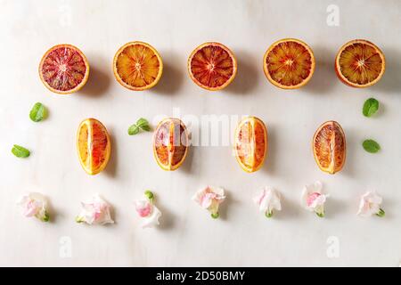 Groupe d'orange sanguine de Sicile bio frais tranchés et son ensemble, les fleurs comestibles, les feuilles de menthe dans la rangée sur fond de marbre blanc. Mise à plat, de l'espace Banque D'Images
