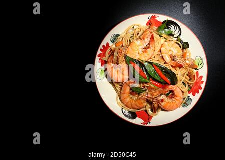 Remuez les spaghettis frits avec de la pâte de Chili, des crevettes, du basilic, du piment frais, des jeunes grains de poivre vert, de l'oignon, des carottes, des feuilles de caffir. Placez une plaque sur un bla Banque D'Images