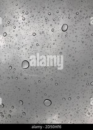 Une collection de gouttelettes de pluie sur le toit ouvrant d'une voiture lors d'une descente de mousson. Banque D'Images