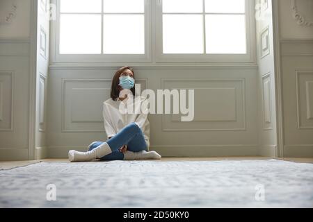 jeune femme asiatique en quarantaine à la maison portant un masque facial assis sur les jambes de plancher croisées, en regardant triste et déprimé Banque D'Images