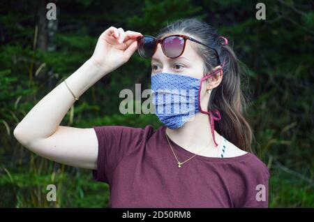 Portrait de la jeune femme avec queue de cheval brun dans un masque réutilisable à motifs colorés sur fond de nature Banque D'Images