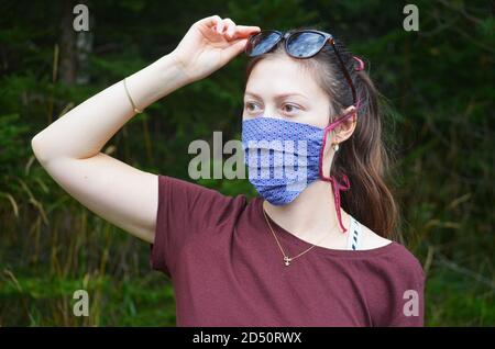 Portrait de la jeune femme avec queue de cheval brun dans un masque réutilisable à motifs colorés sur fond de nature Banque D'Images