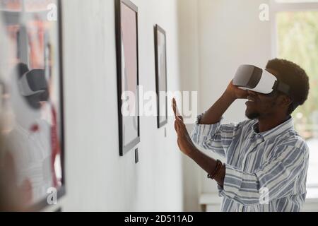 Portrait d'un homme afro-américain souriant portant un équipement VR tout en profitant d'une expérience immersive à l'exposition de la galerie d'art moderne, dans l'espace de copie Banque D'Images
