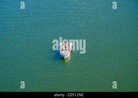 Un pêcheur isolé en uniforme militaire capture du poisson d'un bateau au milieu de la rivière Banque D'Images
