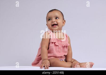 Mignon Indien gai bébé assis et souriant sur blanc. Banque D'Images