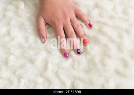 gros plan de la main de la jeune femme avec les ongles peints différentes jolies couleurs une main sur un hiver blanc molletonné arrière-plan Banque D'Images