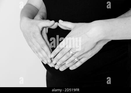 image en noir et blanc de gros plan de l'homme et mains de femme avec anneaux de mariage placés en forme de coeur sur ventre de grossesse Banque D'Images