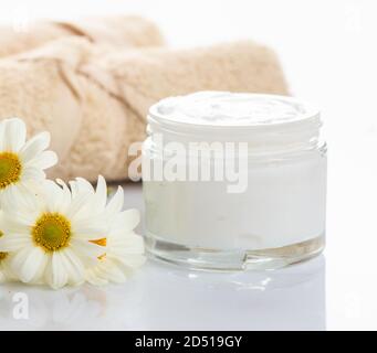 Crème hydratante dans un pot en verre et camomille sur fond blanc. Cosmétiques camomille pour le visage et le corps avec protection aux herbes. Vue rapprochée. Banque D'Images