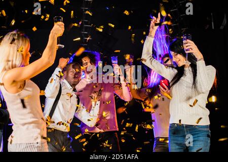 S'amuser ensemble. Groupe de jeunes heureux multi race personnes dansant en tenant le champagne dans des confetti d'or et la vie nocturne souriante nouvelle année celebr Banque D'Images