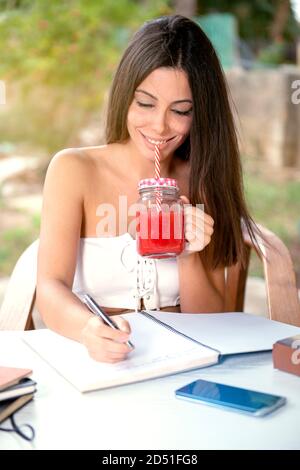 Indépendant travaillant dans le jardin. Écriture, jeune femme se détendant et s'amusant dans la zone du parc boire jus d'orange concept indépendant Banque D'Images