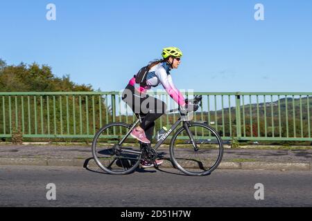 Une femme cycliste à cheval sur une piste cyclable sportive en fibre de carbone Triban sur une route de campagne traversant un pont autoroutier dans la campagne du Lancashire, au Royaume-Uni Banque D'Images