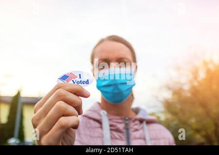 Femme avec masque de visage montrant j'ai voté autocollant aux élections américaines dehors. Banque D'Images