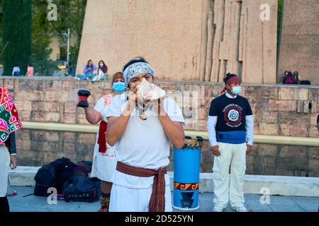 Homme avec un bandana blanc souffle une conque tandis qu'un autre participant tient un encensoir, tambour bleu en arrière-plan, Plaza de Colon, Madrid, 2020 Banque D'Images