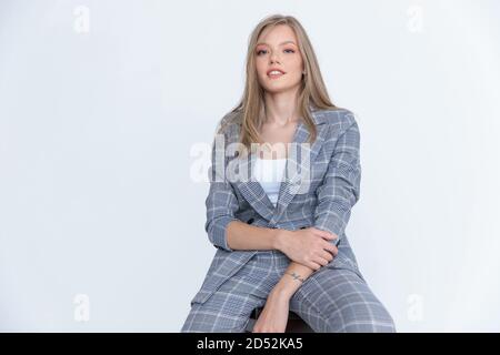 Belle femme d'affaires souriant et posant tout en étant assise dans un studio blanc arrière-plan Banque D'Images