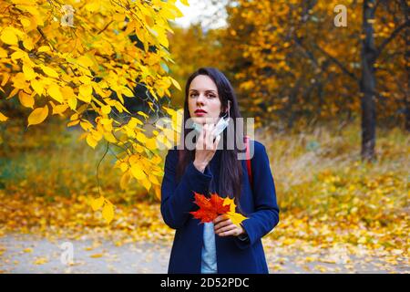 Brunette femme caucasienne tirant vers le bas masque de médecine dans le parc d'automne coloré. Banque D'Images