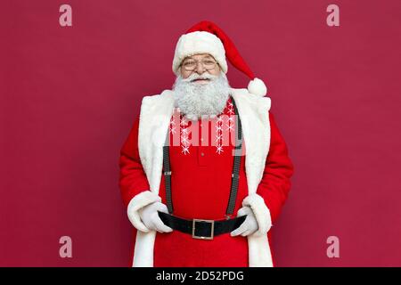 Portrait du vieux Père Noël heureux portant un costume isolé sur fond rouge. Banque D'Images