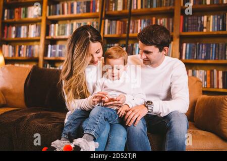 Belle famille avec bébé fils vêtus dans les mêmes vêtements ont l'amusement sur le canapé à la maison pendant Noël. Concept de Noël familial. Parents heureux avec mignon Banque D'Images