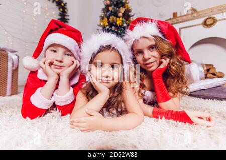 Les enfants en costumes rouges du père noël se trouvent près de l'arbre de noël. Banque D'Images