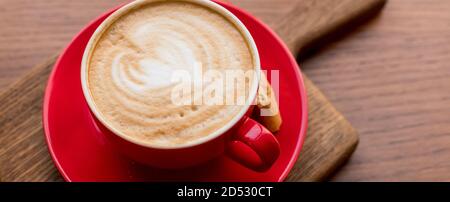 Latte Art, vue latérale du café chaud isolé sur fond de bois. Le matin avec une tasse de café ou de cappuccino rouge. Café d'art et d'artisanat. Bannière web Banque D'Images