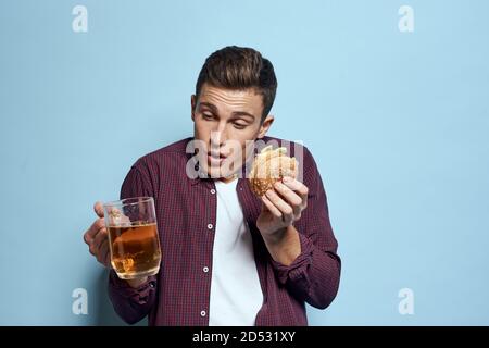 homme gai ivre avec une tasse de bière et un hamburger à la main régime alimentaire style de vie fond bleu Banque D'Images