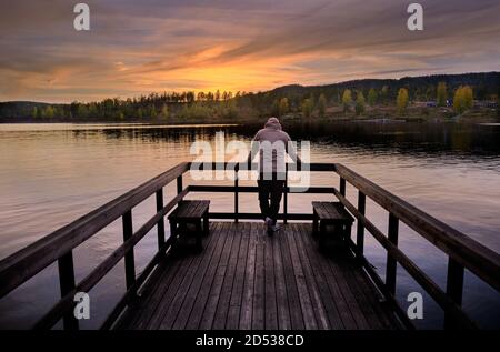 Un homme se tient sur une jetée et donne sur la mer, le coucher de soleil et la forêt dans les couleurs de l'automne Banque D'Images