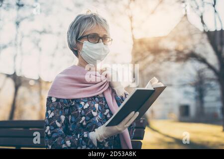 Dame senior avec masque de visage lisant la bible devant une église Banque D'Images