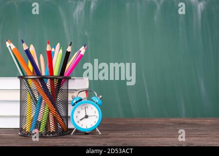 Concept d'éducation scolaire. Photo en gros plan de la pile de crayons de texte et de l'horloge bleue isolée sur le tableau noir vert et la table en bois Copyspace Banque D'Images