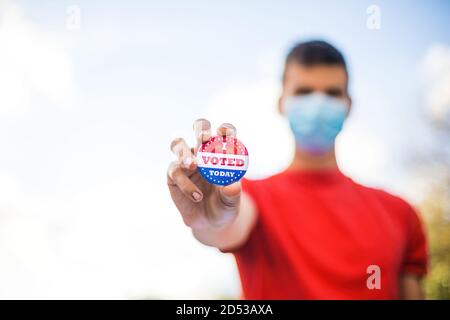 Homme avec masque de visage montrant j'ai voté aujourd'hui badge à l'urne. Banque D'Images