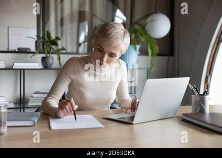 Une femme d'affaires ciblée lit un document fonctionnant avec un ordinateur portable Banque D'Images