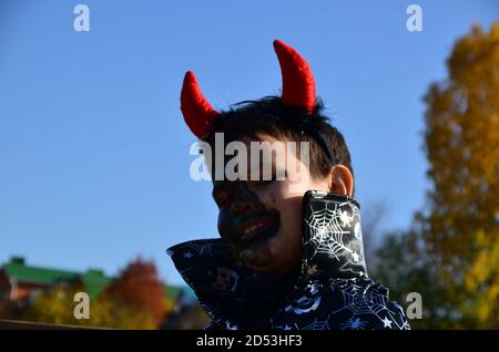 drôle de bébé en diable costume d'halloween avec cornes et trident sur un fond de garçon en bois foncé avec maquillage noir pour halloween, zombie Banque D'Images
