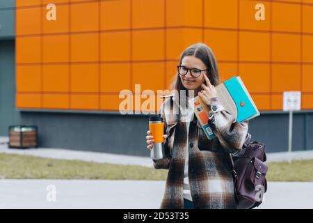 femme étudiante à l'université tenant des cahiers souriants debout sur le campus universitaire. femme heureuse dans les bretelles et les lunettes éducation apprentissage lycée progr Banque D'Images