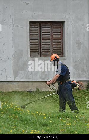 IVANOVO, SERBIE - 16 avril 2018 : travailleur de tondeuse à gazon coupant de l'herbe dans un champ vert avec un coupe-herbe Banque D'Images