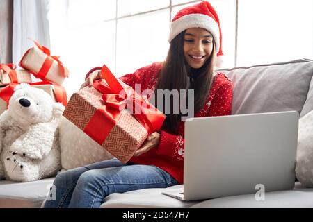 Bonne fille indienne porter chapeau de père noël tenant cadeau d'appel vidéo famille sur Noël. Banque D'Images