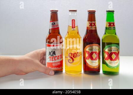 Calgary, Alberta, Canada. 12 octobre 2020. Une personne tenant une bière mexicaine avec diverses bières populaires du Mexique. Bouteilles de bière Tecate, sol, dos Equis Banque D'Images