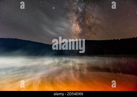 Ciel sombre de nuit avec une façon laiteuse dans le lac Spruce Knob En Virginie occidentale avec la brume jaune rouge montante de l'eau et reflet de la vue sur le paysage des étoiles Banque D'Images