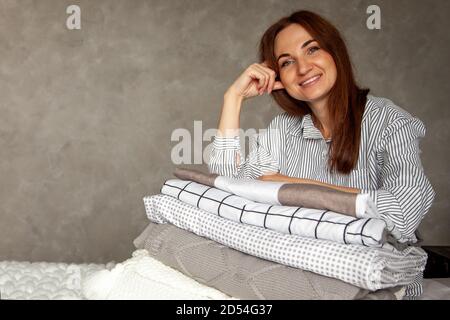 Belle femme en hiver robe chaude épaisse est assis et linge de lit et serviettes de bain soigneusement pliables Banque D'Images
