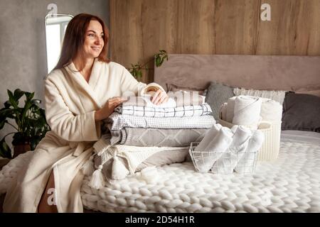 Belle femme en hiver robe chaude épaisse est assis et linge de lit et serviettes de bain soigneusement pliables Banque D'Images