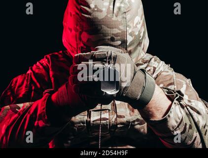 Photo d'un militaire en uniforme et casque armure assis et tenant un collier d'armée en métal sur fond rouge. Banque D'Images